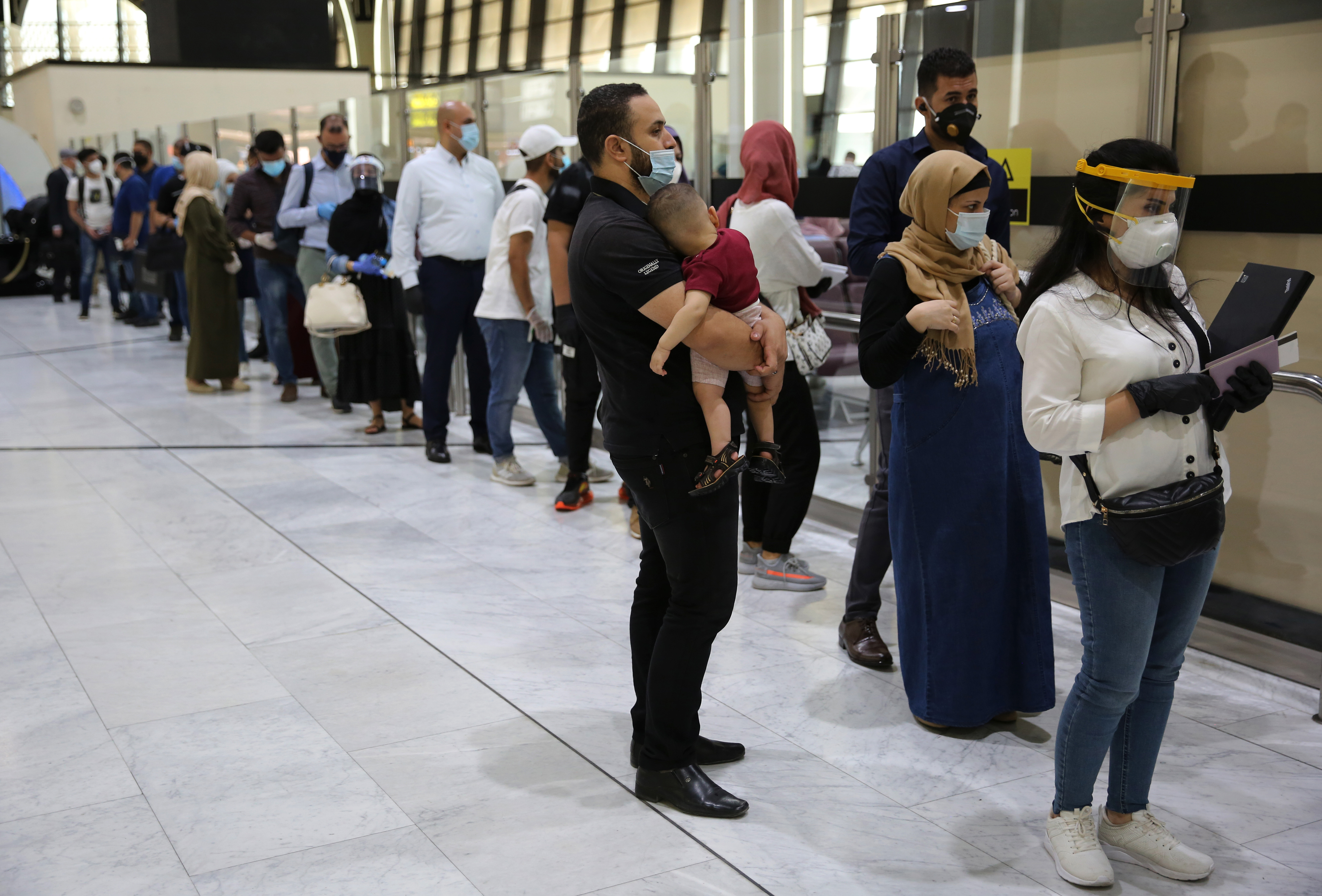 Passengers wearing protective masks wait in line to check in for their flights at the departure hall of Baghdad International Airport, July 23, 2020. (Photo: AFP/Ahmad al-Rubaye)