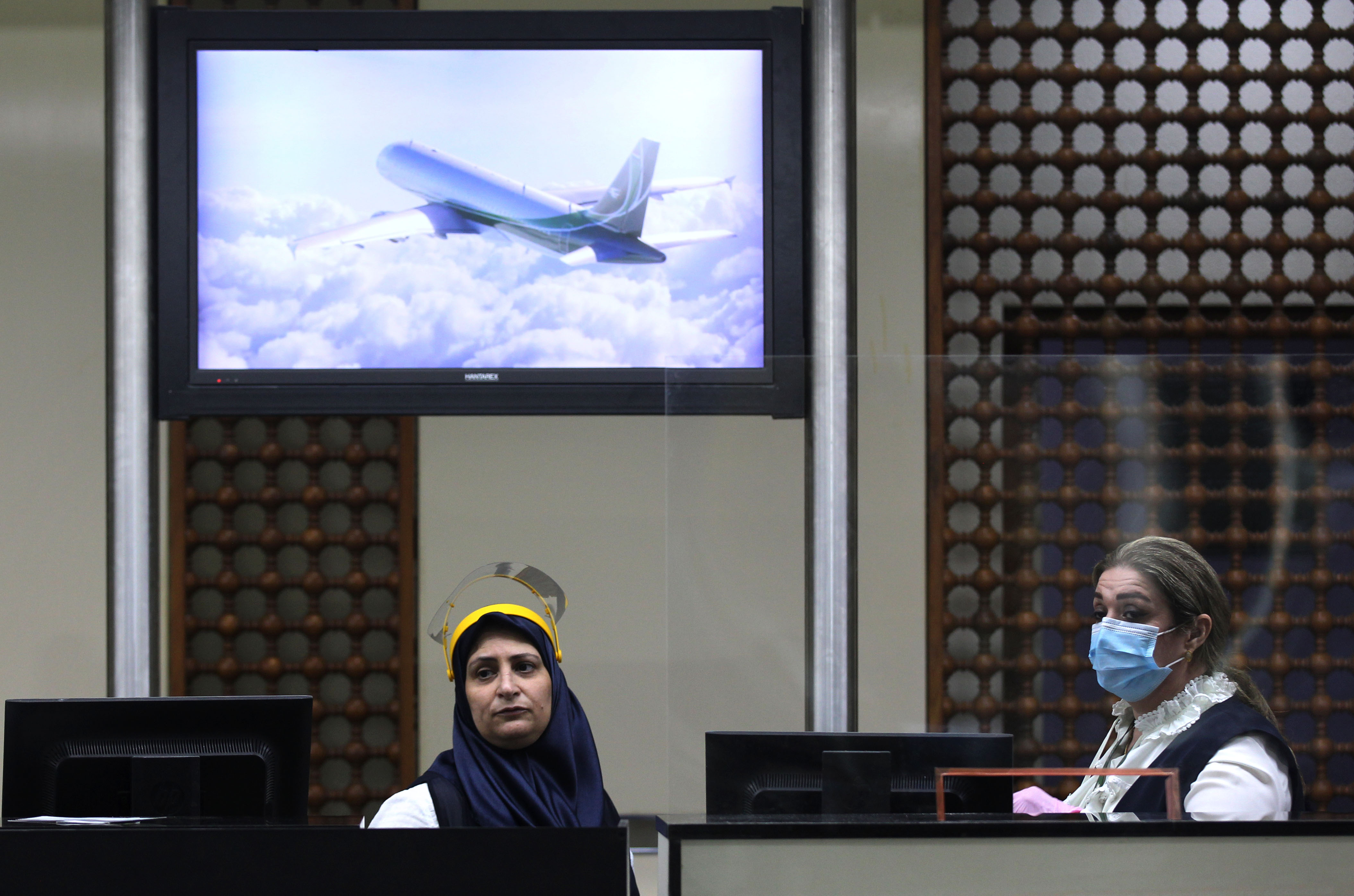 Airline staff, one wearing a protective mask and the other without, assist passengers boarding flights at the departure hall of Baghdad International Airport, July 23, 2020. (Photo: AFP/Ahmad al-Rubaye)