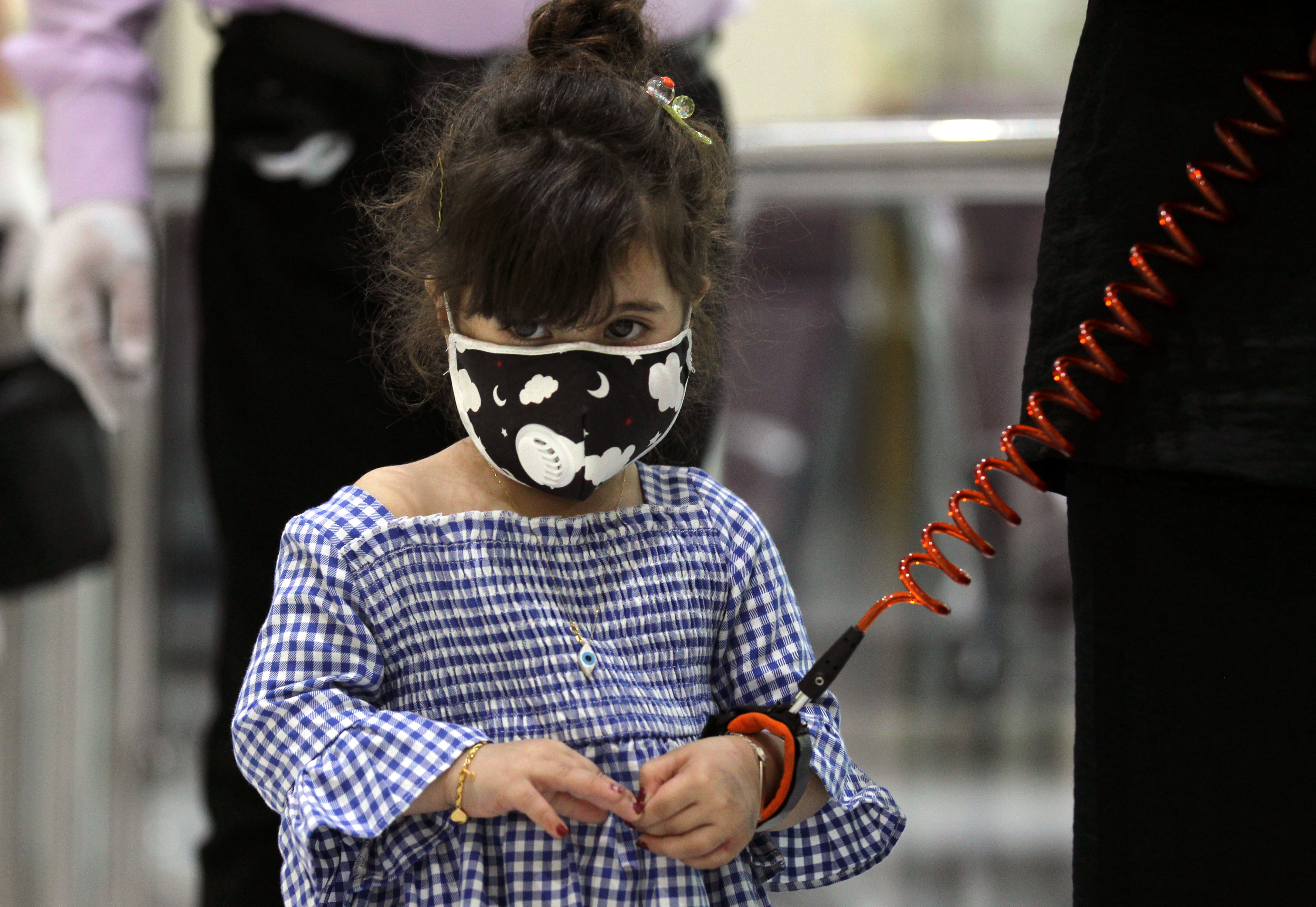 A girl wearing a protective mask and a child safety leash waits with members of her family to board a flight at Baghdad International Airport, July 23, 2020. (Photo: AFP/Ahmad al-Rubaye)