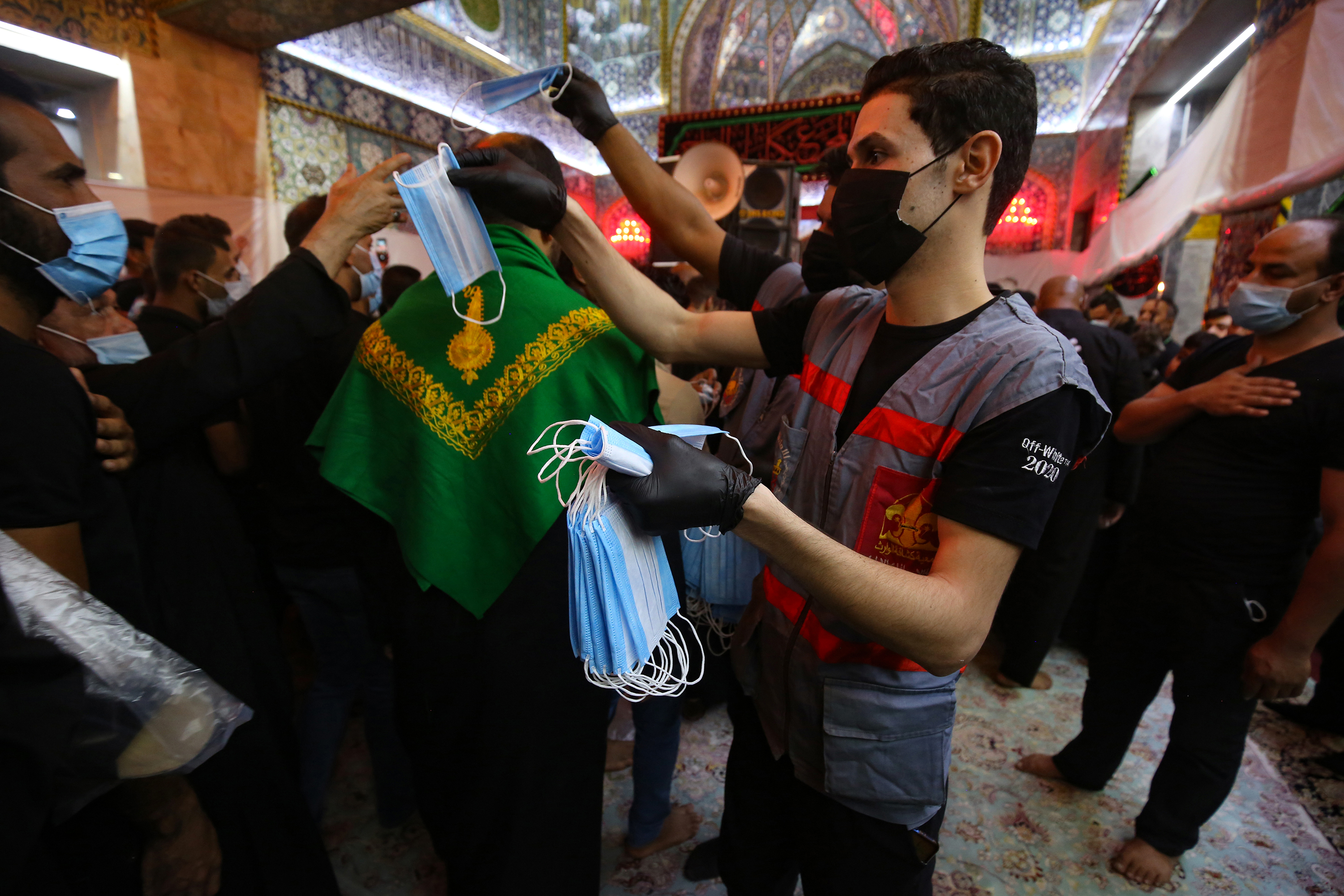 A worker distributes face masks amid the COVID-19 pandemic as Shia Muslim worshippers gather at the Imam al-Abbas Shrine to commemorate the martyrdom of Prophet Mohammad's grandson Imam Hussein, during the Islamic month of Muharram in Iraq's central holy city of Karbala. (Photo: Ahmad al-Rubaye/AFP)